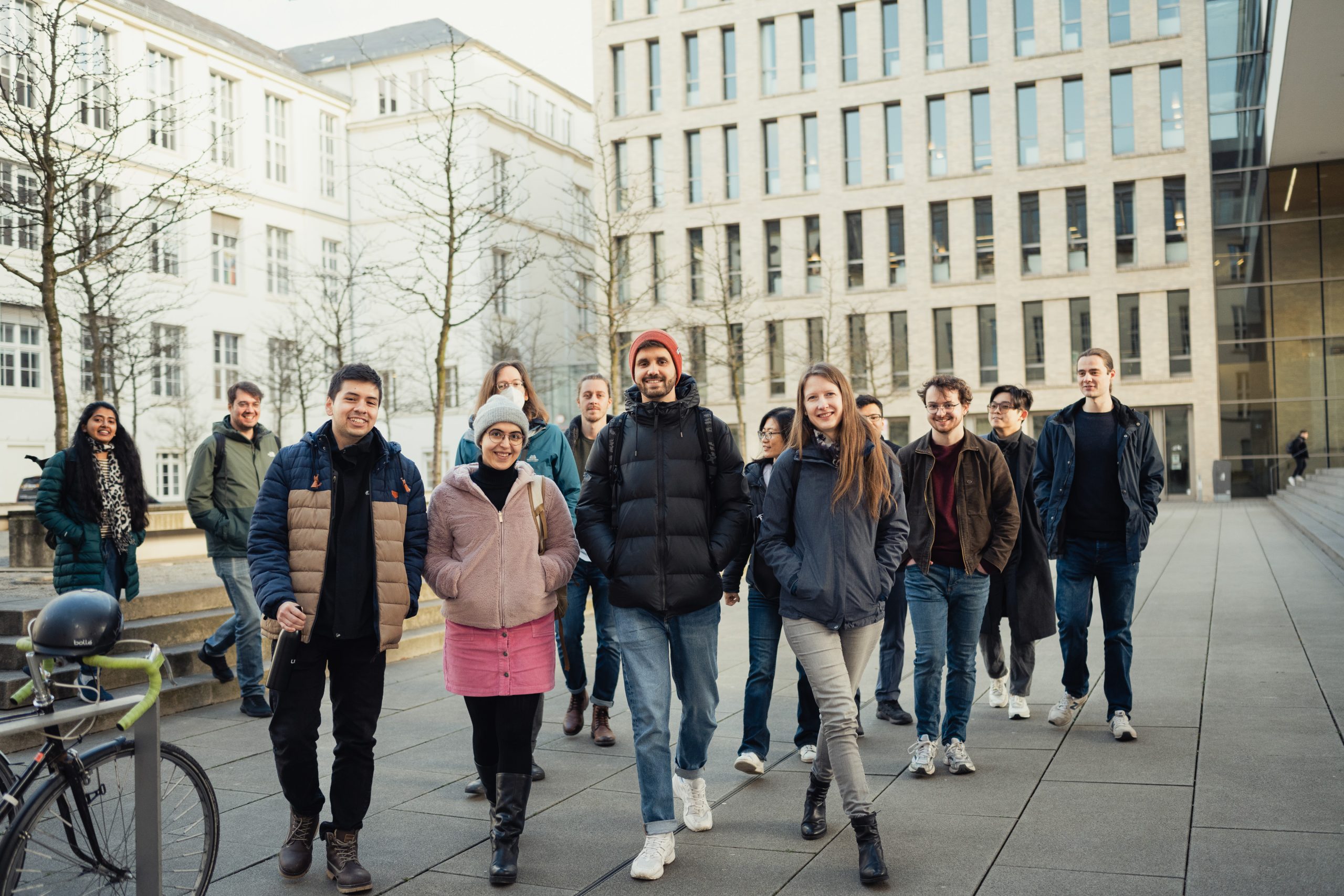 Diverse group of students walking together on a university campus plaza between modern academic buildings, representing community and collaboration in higher education.